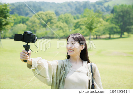 A plainclothes woman taking a V-log selfie in the park 104895414