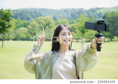 A plainclothes woman taking a V-log selfie in the park 104895420
