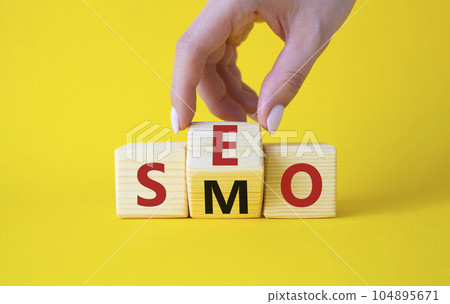 SEO vs SMO symbol. Businessman hand turns wooden cubes and changes the word SMO to SEO. Beautiful yellow background. SEO vs SMO and business concept. Copy space 104895671