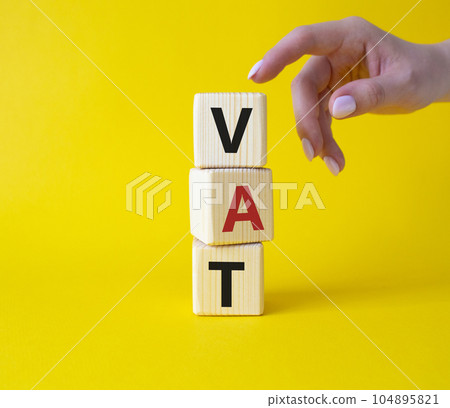 VAT - Value Added Tax symbol. Wooden cubes with word VAT. Businessman hand. Beautiful yellow background. Business and Value Added Tax concept. Copy space. VAT - Value Added Tax symbol. Wooden cubes with word VAT. Businessman hand. Beautiful yellow background. Business and Value Added Tax concept. Copy space. 104895821
