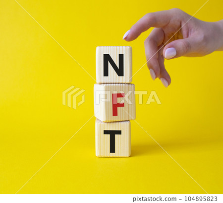 NFT - non-fungible token symbol. Concept word NFT on wooden cubes. Businessman hand. Beautiful yellow background. Business and NFT concept. Copy space. NFT - non-fungible token symbol. Concept word NFT on wooden cubes. Businessman hand. Beautiful yellow background. Business and NFT concept. Copy space. 104895823