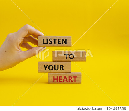 Listen to your heart symbol. Concept word Listen to your heart on wooden blocks. Beautiful yellow background. Businessman hand. Business and Listen to your heart concept. Copy space 104895868