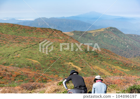 Climbers resting and Mt. Kurikoma in autumn leaves Climbers resting and Mt. Kurikoma in autumn leaves 104896197
