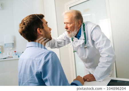 Close-up of mature adult male ophthalmologist examining eyes of male patient during checkup visit in clinic office. Young man coming in for consultation before undergoing vision correction surgery. 104896204