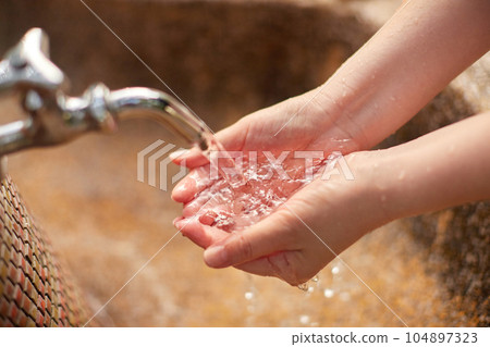 The hands of a woman washing her hands with tap water in the garden The hands of a woman washing her hands with tap water in the garden 104897323