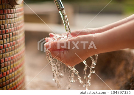 The hands of a woman washing her hands with tap water in the garden The hands of a woman washing her hands with tap water in the garden 104897325