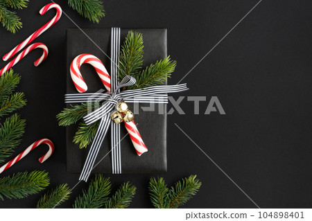 Christmas black gift box with candy cane, bells and spruce twigs on dark background. Space for your text 104898401