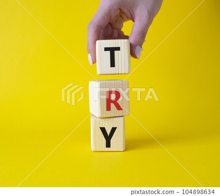 Try symbol. Wooden cubes with word Try. Businessman hand. Beautiful yellow background. Business and Try concept. Copy space. Try symbol. Wooden cubes with word Try. Businessman hand. Beautiful yellow background. Business and Try concept. Copy space. 104898634