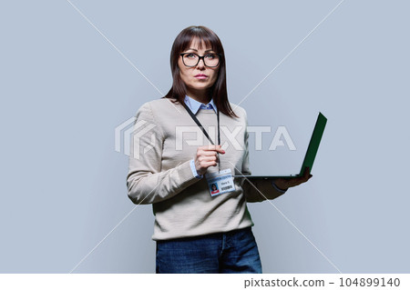 Middle aged confident serious female teacher using laptop on grey background Middle aged confident serious female teacher using laptop on grey background 104899140