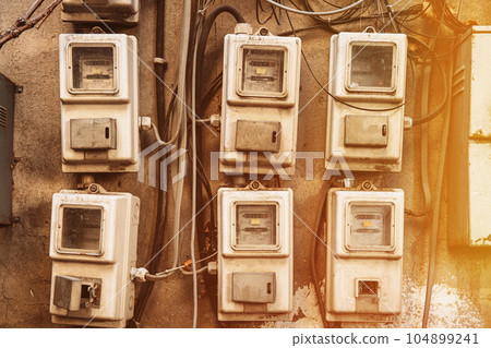 Various Electric Meters Stand A Row. Energy Consumption Concept. Impact On Environment. Dial Electric Power Meters Measuring Power Usage. Need For Saving Energy. Electricity Meter Measures Current 104899241
