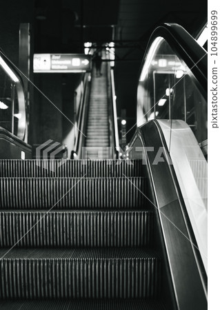 Vertical grayscale shot of metro escalator stairs in a german subway Vertical grayscale shot of metro escalator stairs in a german subway 104899699
