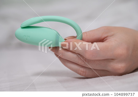 Woman holding mint vibrator while lying on white sheet. Woman holding mint vibrator while lying on white sheet. 104899737