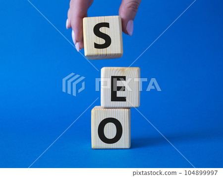 SEO - Search Engine Optimization symbol. Wooden blocks with words SEO. Businessman hand. Beautiful blue background. Business and SEO concept. Copy space. SEO - Search Engine Optimization symbol. Wooden blocks with words SEO. Businessman hand. Beautiful blue background. Business and SEO concept. Copy space. 104899997