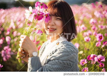 波斯菊花田裡拿著花束微笑的女人 104900348