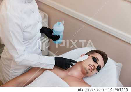 Young man receiving epilation in beauty center. laser hair removal procedure 104901303