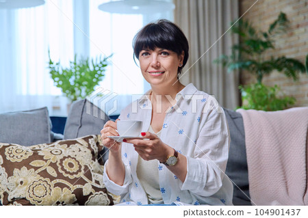 Smiling mature woman relaxing at home with cup of coffee tea Smiling mature woman relaxing at home with cup of coffee tea 104901437