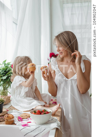 A little blonde girl with her mom on a kitchen countertop decorated with peonies. The concept of the relationship between mother and daughter. Spring atmosphere. A little blonde girl with her mom on a kitchen countertop decorated with peonies. The concept of the relationship between mother and daughter. Spring atmosphere. 104902047