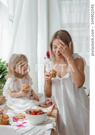 A little blonde girl with her mom on a kitchen countertop decorated with peonies. The concept of the relationship between mother and daughter. Spring atmosphere. A little blonde girl with her mom on a kitchen countertop decorated with peonies. The concept of the relationship between mother and daughter. Spring atmosphere. 104902048