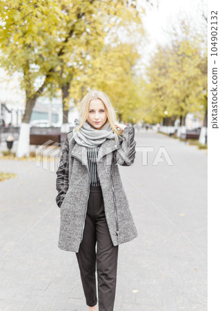 A young blonde walks through the autumn city in a gray coat. The concept of urban style and lifestyle. A young blonde walks through the autumn city in a gray coat. The concept of urban style and lifestyle. 104902132