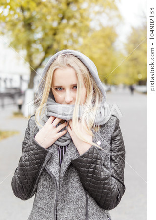 A young blonde walks through the autumn city in a gray coat. The concept of urban style and lifestyle. A young blonde walks through the autumn city in a gray coat. The concept of urban style and lifestyle. 104902133