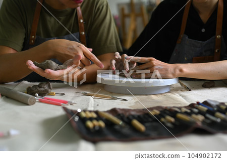 Cropped image of master ceramist teaches helping student creating plate handmade from clay in art workshop Cropped image of master ceramist teaches helping student creating plate handmade from clay in art workshop 104902172