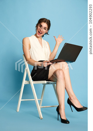 Portrait of cheerful young woman, employee working online on laptop against blue studio background. Business meeting Portrait of cheerful young woman, employee working online on laptop against blue studio background. Business meeting 104902293