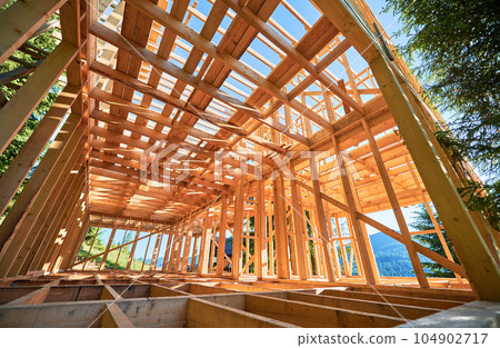 Under-construction residential wooden frame home located near a forest. Commencement of a new construction project for a cozy house or a mountain cottage. Idea of contemporary ecological construction. 104902717