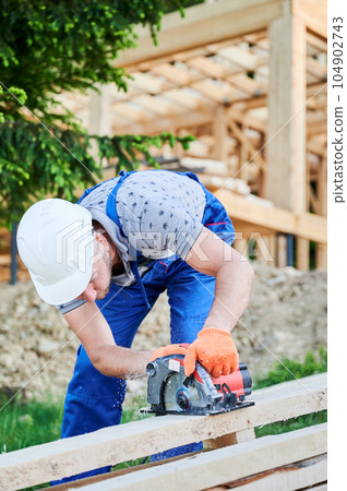 Carpenter using circular saw for cutting wooden plank. Man worker building wooden frame house. The ideology behind modern, environmentally-conscious construction. 104902743