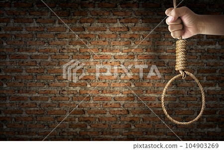 Hand holding rope noose with hangman's knot hanging on dark brick wall Hand holding rope noose with hangman's knot hanging on dark brick wall 104903269