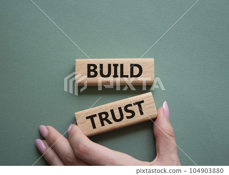Build trust symbol. Wooden blocks with words Build trust. Beautiful grey green background. Businessman hand. Business and Build trust concept. Copy space. Build trust symbol. Wooden blocks with words Build trust. Beautiful grey green background. Businessman hand. Business and Build trust concept. Copy space. 104903880