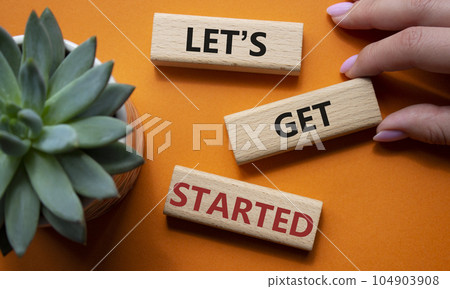 Lets get started symbol. Concept words Lets get started on wooden blocks. Beautiful orange background. Businessman hand. Business and Lets get started concept. Copy space. Lets get started symbol. Concept words Lets get started on wooden blocks. Beautiful orange background. Businessman hand. Business and Lets get started concept. Copy space. 104903908