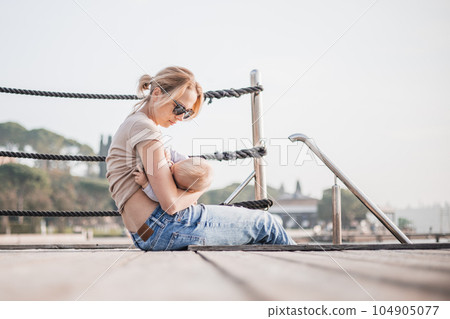 Mother breast feeding her little baby boy infant child on old wooden pier by the sea on nice warm spring day enjoing nature and warm breeze outdoors Mother breast feeding her little baby boy infant child on old wooden pier by the sea on nice warm spring day enjoing nature and warm breeze outdoors 104905077