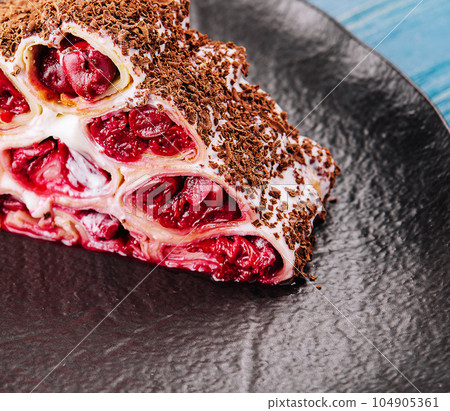 Cake from rolled pancakes with cream, cherries and grated chocolate 104905361