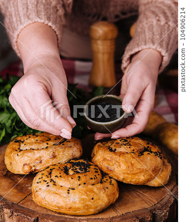 woman sprinkles seeds fresh twisted bun with sesame seeds 104906214
