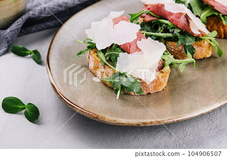 Bruschetta with beef, arugula and parmesan cheese 104906507