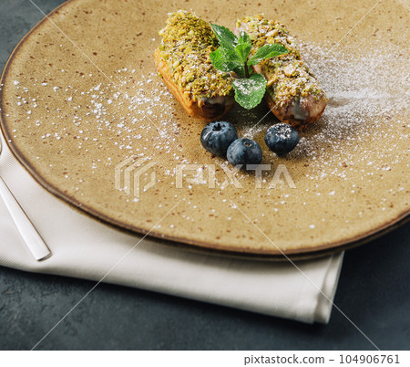 Tasty eclairs with pistachios and cheesecake on plates Tasty eclairs with pistachios and cheesecake on plates 104906761