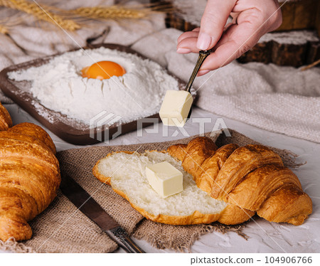woman hands cut a fresh croissant and spreading butter woman hands cut a fresh croissant and spreading butter 104906766