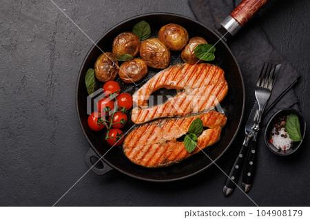 Grilled salmon steaks and potatoes sizzling in a frying pan Grilled salmon steaks and potatoes sizzling in a frying pan 104908179