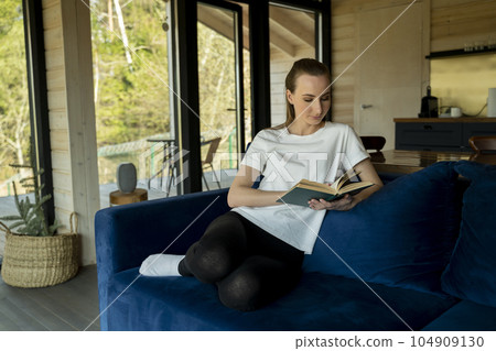 Attractive young woman sits in the minimal and comfortable living room enjoying reading a book. 104909130