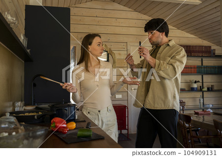 Infidelity. A jealous husband shows his cheating wife her phone, demanding an explanation, standing in the kitchen. Husband caught his wife cheating with a mobile phone - divorcing people 104909131