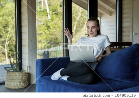 A picture of a pretty woman celebrating something while working with a laptop, sitting at home on a blue sofa A picture of a pretty woman celebrating something while working with a laptop, sitting at home on a blue sofa 104909139