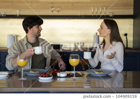 Married couple, a serving table with full dishes, a welcome dinner, a young couple chatting in the living room indoors Married couple, a serving table with full dishes, a welcome dinner, a young couple chatting in the living room indoors 104909159