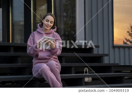 Young woman is working with a tablet while sitting on the stairs of her house on a beautiful summer day 104909319