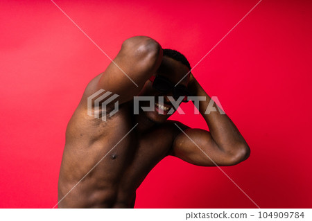 Portrait of an athletic african american man topless smiling, yellow, red and black background 104909784