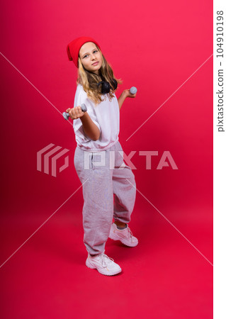 Kid girl doing fitness exercises with dumbbells on red background Kid girl doing fitness exercises with dumbbells on red background 104910198