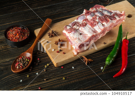 Fresh raw chopped pork ribs on a kitchen cutting board with spices and hot peppers. Cooking delicious food at home Fresh raw chopped pork ribs on a kitchen cutting board with spices and hot peppers. Cooking delicious food at home 104910517