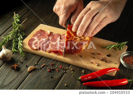 The chef cuts the baked veal meat with a knife for cooking dinner in the kitchen. Fast street food concept on dark background 104910533