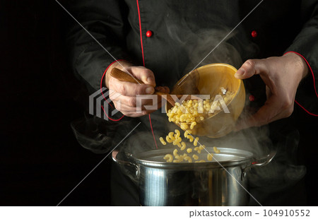 The cook spoons the pasta into the pan. Dark space for recipe or menu. The idea of cooking delicious pasta in the restaurant kitchen 104910552