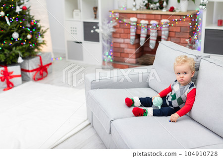 A child sits on the couch and waits for presents from under the Christmas tree 104910728