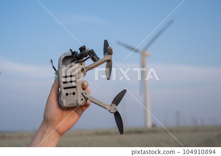 Woman holding a crashed drone against the backdrop of windmills. Woman holding a crashed drone against the backdrop of windmills. 104910894